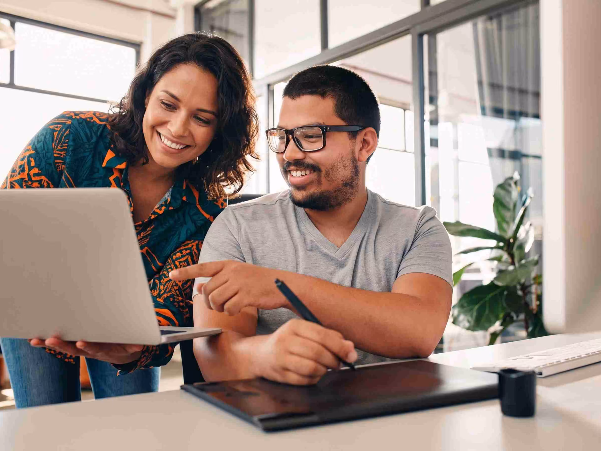 Duas pessoas num escritório olham juntas a tela de um notebook